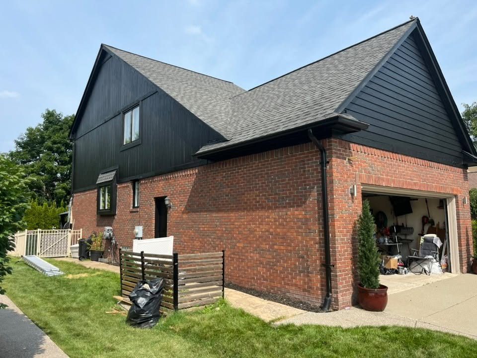 The finished home with deep black board-and-batten siding and gables above the untouched red brick, with crisp black window trim