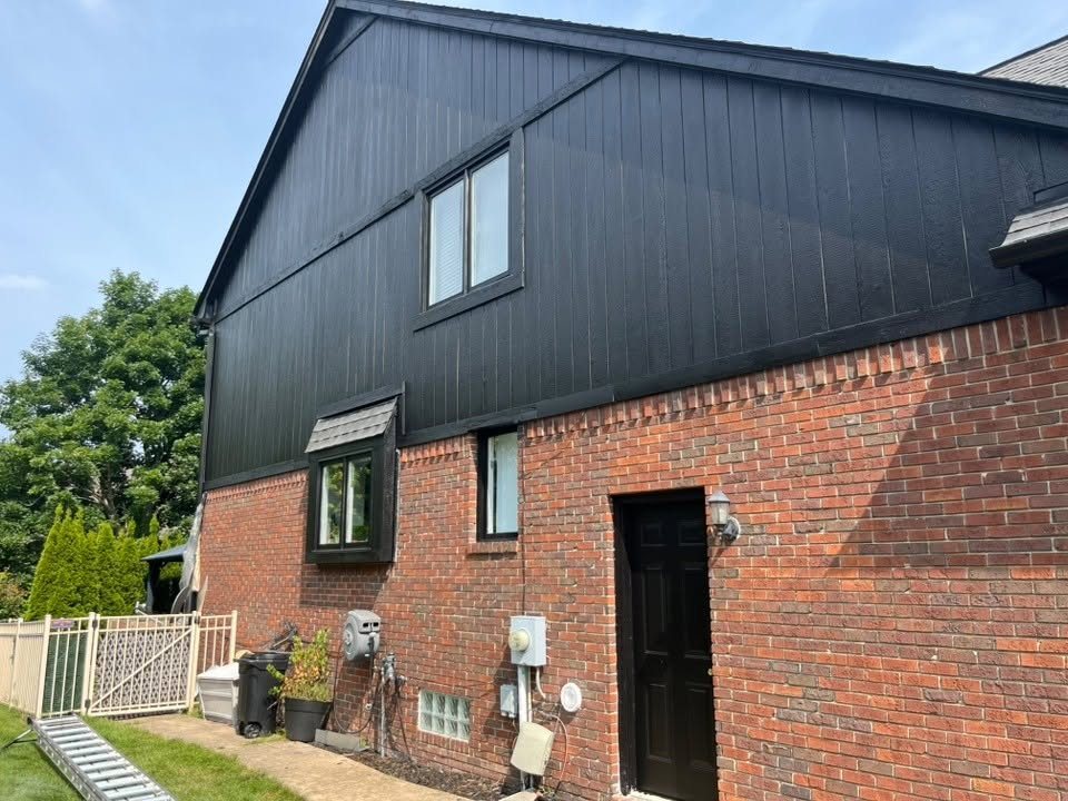 Black board-and-batten siding meeting red brick on the side of a finished two-story home