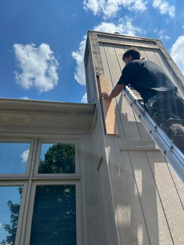 An UpLife Painting crew member on an extension ladder replacing a damaged siding board high on a gable before painting begins