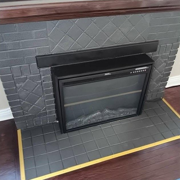 A brick fireplace surround painted a soft grey, with the hearth taped off in yellow