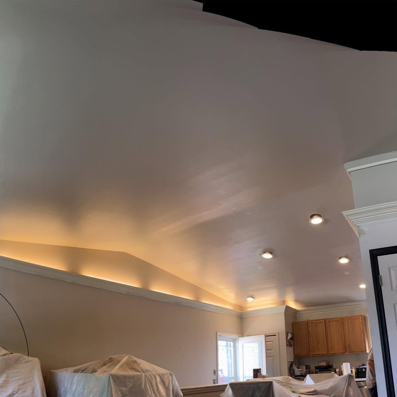 A freshly painted vaulted living-room ceiling with the furniture below covered in drop cloths