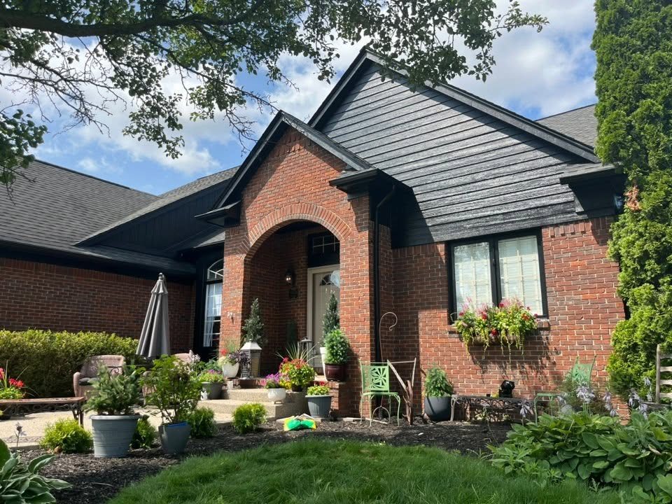 A brick ranch home with its gables, soffits and trim finished in deep charcoal, flower beds in front