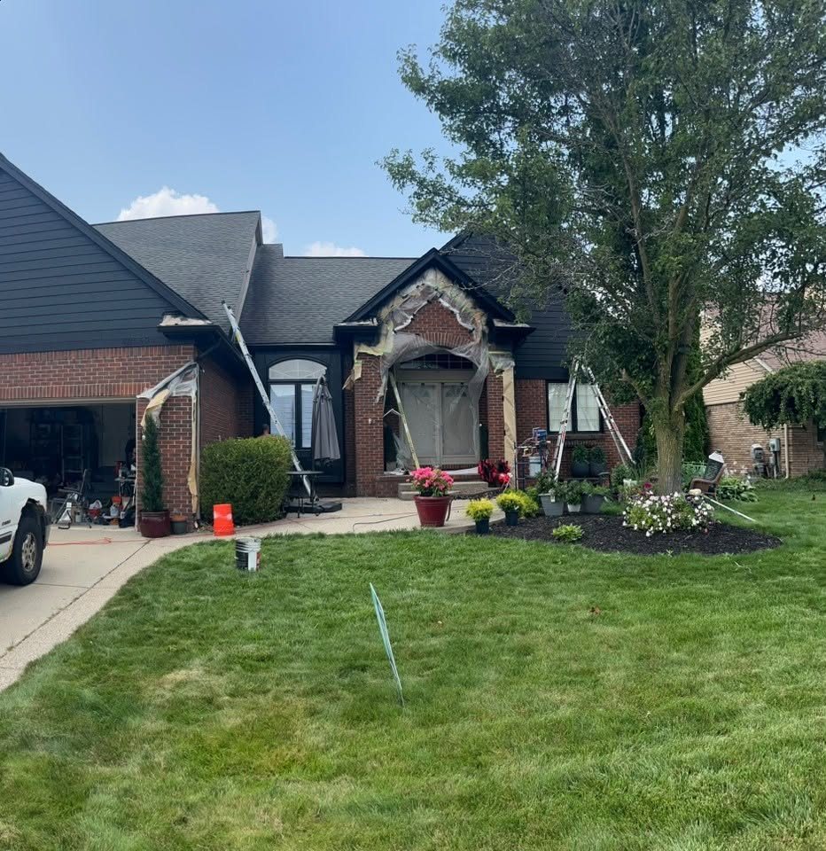 The brick ranch mid-project with ladders up, the arched entry and window trim papered and plastic-masked, and a work truck in the driveway